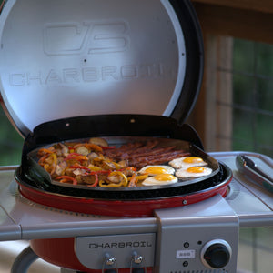 Red Char-Broil grill with open lid, cooking eggs, bacon, peppers, and potatoes.