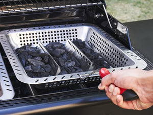 Hand placing charcoal tray with divider into Char-Broil grill for even heat distribution.