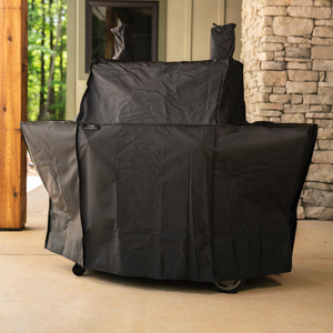 Black outdoor grill cover with wheels, protecting a grill.