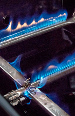 Blue gas burner with flame, part of a stainless steel appliance.