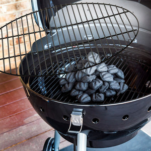 Black charcoal briquettes in a black Weber kettle grill with lid open.