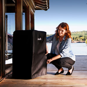 Black Char-Broil grill cover on wooden deck near water.