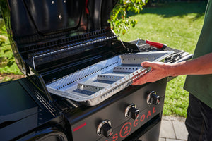 Person placing a charcoal tray inside a Char-Broil Gas2Coal grill outdoors, preparing for grilling.